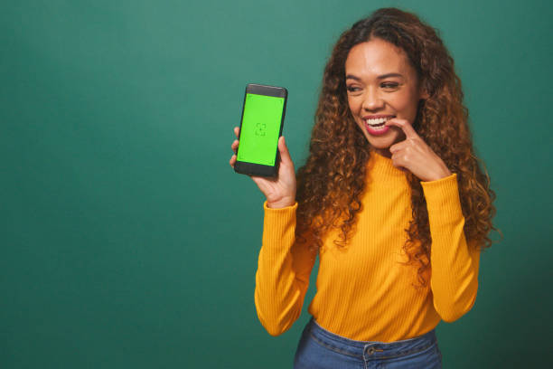 istock Happy young woman holds up device chroma key screen, green studio background 1674116421