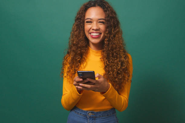 istock Beautiful young woman texting on cellphone, smiling, green studio background 1674118587