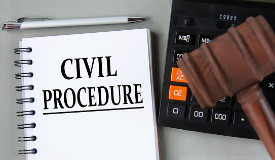 CIVIL PROCEDURE - words in a white notebook on the background of a calculator and a judge's gavel