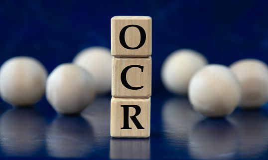 OCR (Optical Character Recognition) - acronym on wooden cubes on a blue background with wooden balls. Info concept