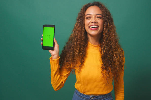 istock Happy young woman holds up device chroma key screen, green studio background 1674137209
