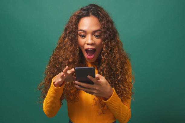 istock Young biracial woman reads text message shocked wow, green studio background 1674137215