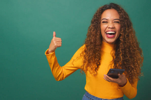 istock Beautiful young woman points thumb to copy space left, cellphone, green studio 1674137226