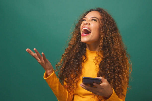 istock Young biracial woman celebrates after reading text wow, green studio background 1674138928