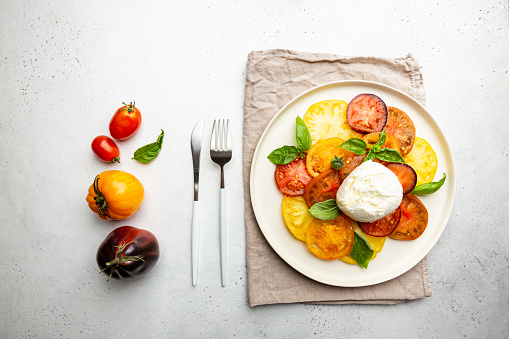Delicious caprese salad with ripe colorful tomatoes and mozzarella cheese with fresh basil leaves. Italian food, top view