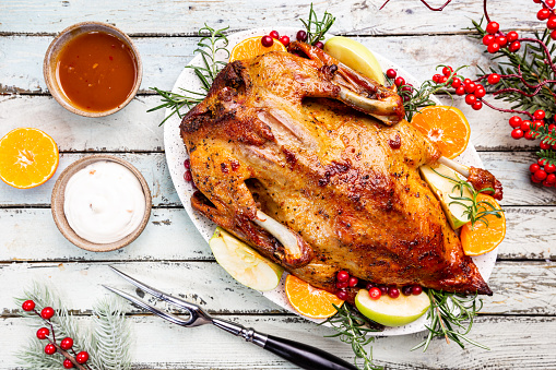 Baked duck with apples and oranges served with sauces, over white wooden background, top view. Christmas festive table.