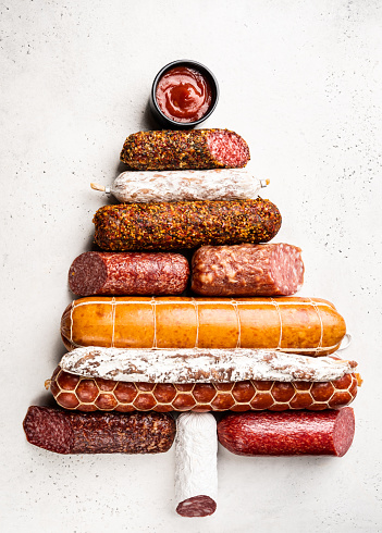 Christmas tree from different types of sausages, salami and smoked meat with basil and spices on white background. Top view.