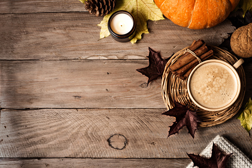 Autumn aesthetic concept. Cup of cappuccino coffee with candle, plaid and maple autumn leaves on wooden background, top view, copy space.