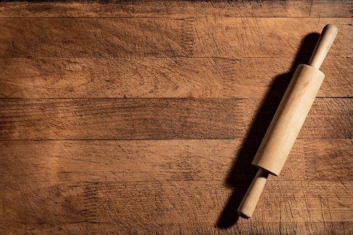 Rolling pin on wooden cutting board or kitchen table, top view, copy space. Baking or cooking concept.