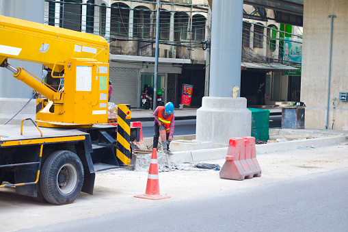 Thai worker with jackhammer on street in Bangkok. Man is working close to a crane truck  below BTS line and station on street Ladprao Road in Bangkok. Scene is at new station of BTS LRT line terminal Chokchai 4.  Man is working in center of street