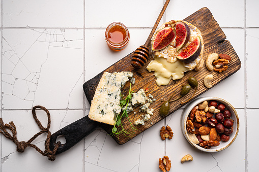 Brie cheese on a wooden Board with fresh figs, gorgonzola and honey over white tail background, top view