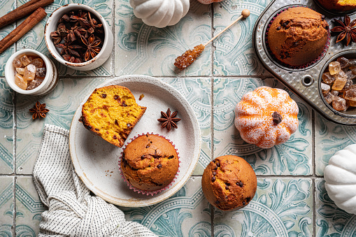 Homemade autumn pumpkin muffins with cinnamon and chocolate on tile background, top view