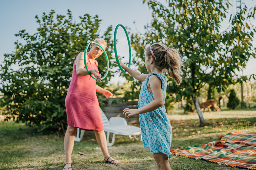 Cute little girl with her mother playing with plastic hoops outdoors in back yard.