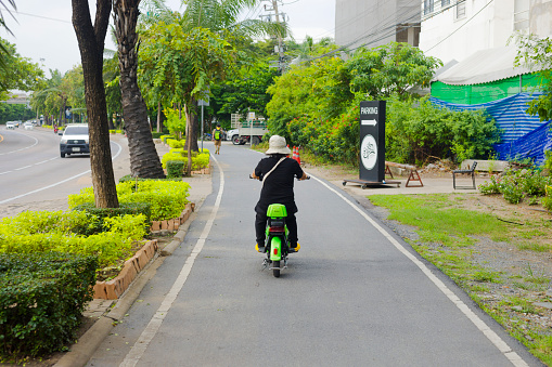 Thai senior woman on electric vehicle on bicycle land of Bicycle land at Praditmanutham Rd in Bangkok. View view of woman on a small electric mofa. Scene is in Wang Thonglang subdistrict