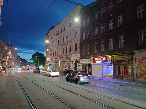 Vienna, Austria - June 7, 2023: Street life in center of Vienna city, Austria with buildings, shops, cars and rail. Cityscape at night.