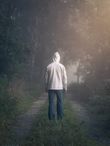 Young man in white hoodie and pants walking through misty fog forest from back