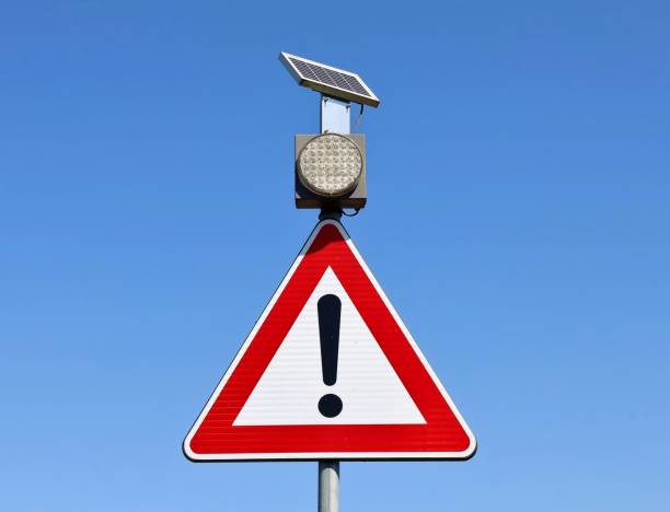Solar panel powered traffic warning light above a triangle warning sign with exclamation point. Solar panel powered traffic warning light above a triangle warning sign with exclamation point. Blue sky background. triangular solar panels stock pictures, royalty-free photos & images