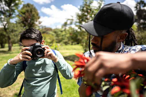 Young man and his friend photographing flowers outdoors