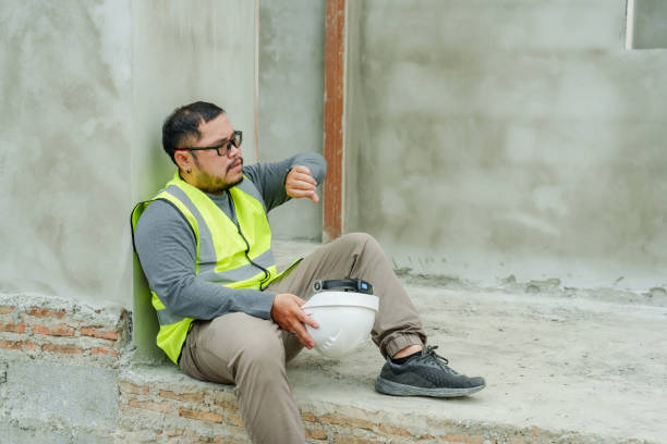 istock Asian architect construction supervisor Take off white safety helmet. Look at the clock and see time when work starts in afternoon. Sitting against a cement wall, taking a break from work, face tired. 1674166860