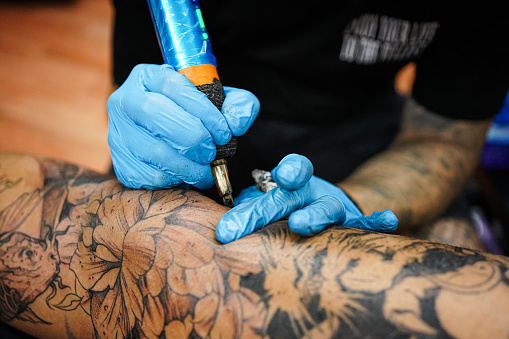 Two men in tattoo studio, man is tattooing a men's leg