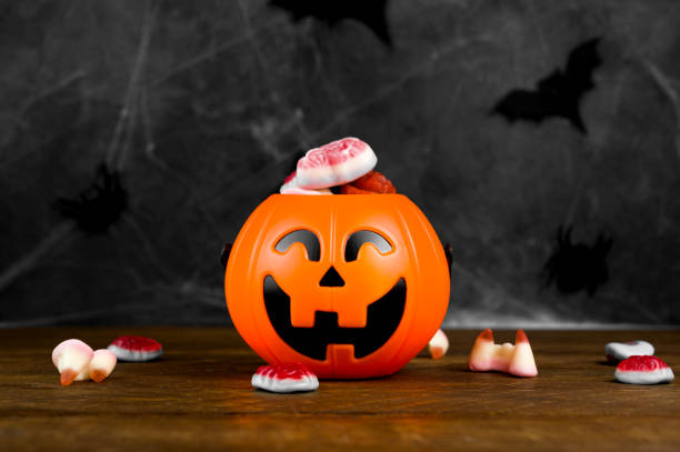 istock Jack'o'lantern shaped candy bowl with delicios scary sweets on dark concrete background decorated with spider web and bats.Trick or treat concept. Halloween celebration. 1674187492
