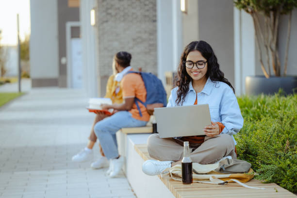 istock Young Latin female student using laptop on the bench on campus 1674214146