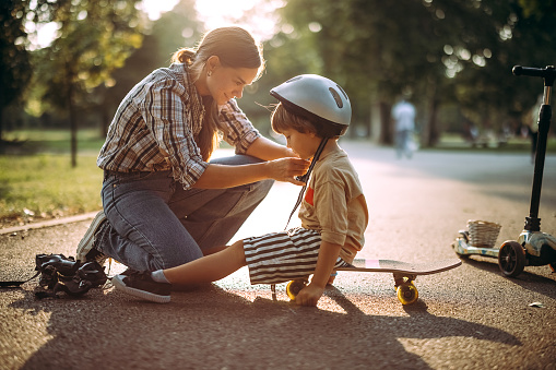 Handsome young mother helps to her cute little son put on sport helmet