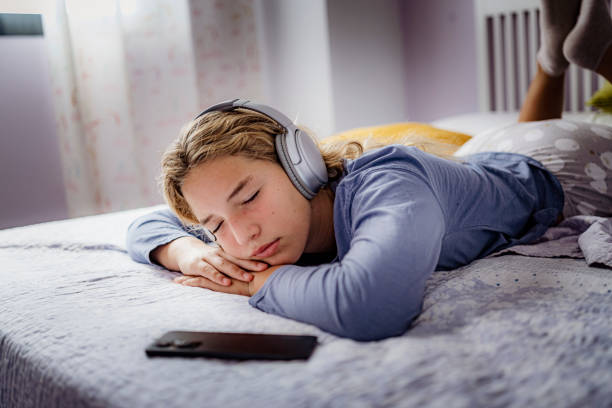 occhi rilassati della ragazza adolescente chiusi ascoltando musica che giace sul davanti nella sua camera da letto - one teenage girl only on the phone bed lying on front foto e immagini stock