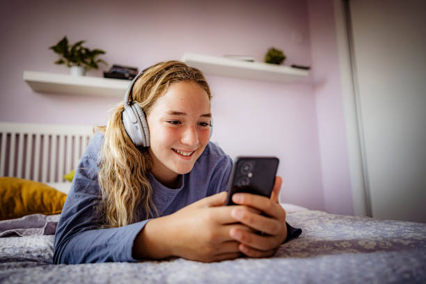 messaggio di testo della ragazza adolescente mentre ascolta la musica - one teenage girl only on the phone bed lying on front foto e immagini stock