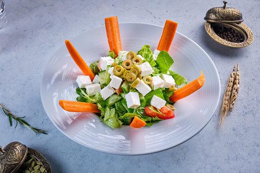 A blate of green salad with cheese and carrots on Gray background