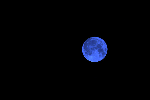 A landscape shot of a white full moon with black color in the background