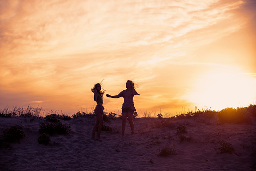 Mother and daughter have fun on the sand beach in sunset. Copy space