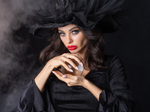 Woman in Halloween witch fortune teller costume with crystal ball. Beautiful sexy model girl in sinister costume and make up