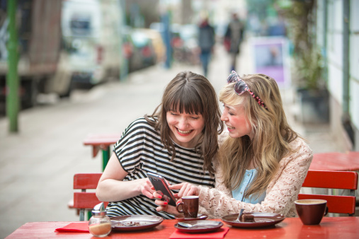 Two women sitting at a cafe table having fun reading from the smartphone.