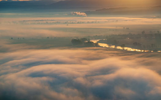 Aerial view of the valley in early morning mist, beautiful in the highlands. Low clouds and fog cover the sleeping meadow. Alpine mountain valley mists landscape at dawn. Serene moment in rural area