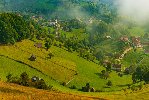 Rural idyllic landscape of the small villages in the Rucar-Bran mountain area, Brasov, Romania, scattered on the wooded hills, with the Bucegi mountains in the background, in wonderful springtime day