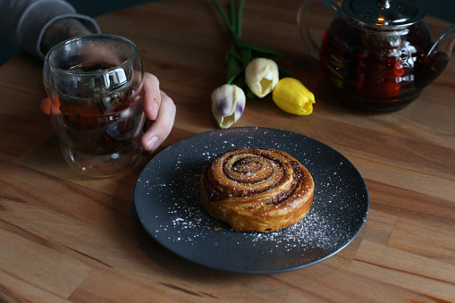 Cinnamon rolls with sugar powder on a black plate on a wooden table.
