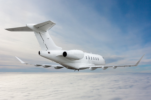 White luxury business jet flying in the air above the clouds