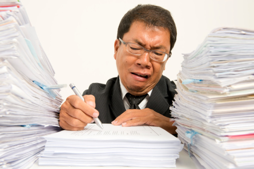 Asian businessman frustrated at pile of undone paperwork