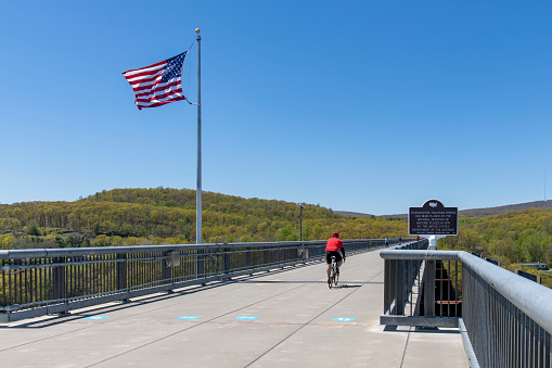 Poughkeepsie, NY, USA-May 2022; View over the 1.28 miles Walkway Over the Hudson State Historic Park Bridge from 1889 with male cyclist passing by; part of the Hudson Valley Rail Trail