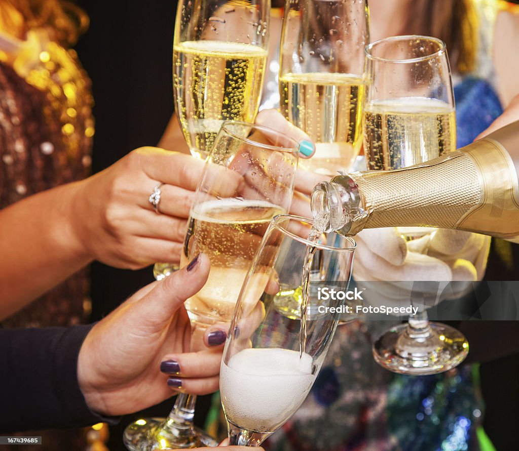 Hands holding champagne glasses during a toast Five hands holding five champagne flutes being clinked together while being filled with champagne from a bottle.  Glittery party clothing can be seen in the background being worn by the people holding the champagne flutes, but the faces of these people can not be seen.  The lighting effect in the image is bright and sparkling. Champagne Stock Photo