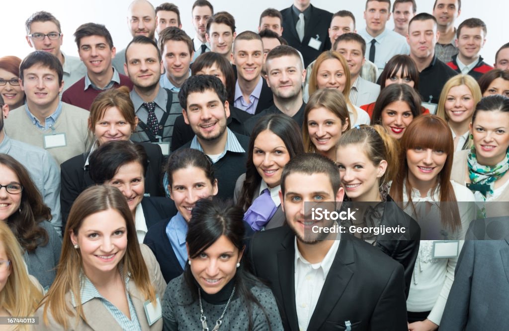 Large group of people smiling in camera A large group of smiling business people are standing in a room and are all facing forward.  It's a mix of young women and men.  They are dressed in business casual clothes and fill up the whole picture. A white background can barely be seen at the top of the picture. Large Stock Photo