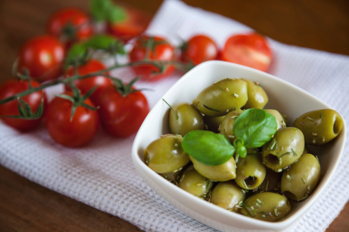 Close up of herb marinated olives with tomatoes beside.