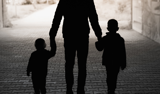 Silhouette of father parent holding hands with children walking through a tunnel.