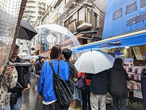 Chuo Ward, Japan - May 23, 2023: Shoppers visit the famous Tsukiji Outer Market near the Sumida River. Spring morning with rain in the Tokyo Metropolis.
