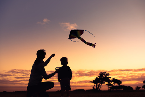 Mother and son flying kite at sunset.