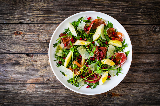 Tasty salad - ham, parmesan, pear and fresh vegetables on wooden table