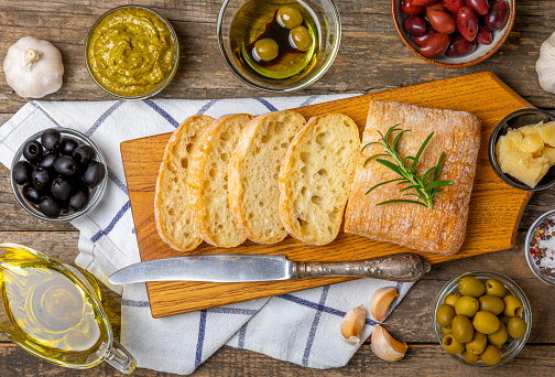 Italian ciabatta bread cut in slices with herbs, olives, pesto sauce, garlic and parmesan cheese on a concrete table. Fresh homemade Italian Ciabatta bread sliced with herbs and spices.Place for text.
