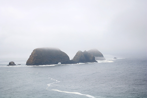 Color landscape photograph of the Three Arch Rocks sea stack rocks in the Fog taken from the view on the beach near Cape Mears in coastal Oregon.