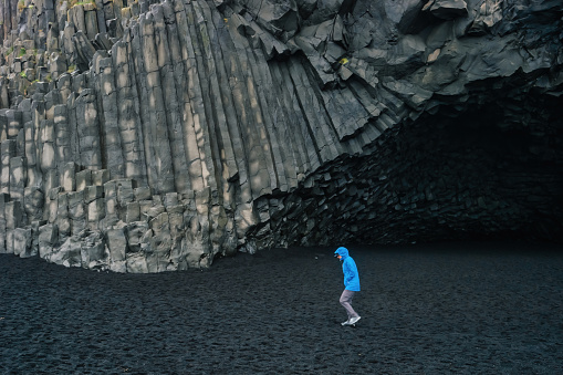 Woman hikes below dramatic basalt columns at Reynisfjara Black Sand Beach , Iceland